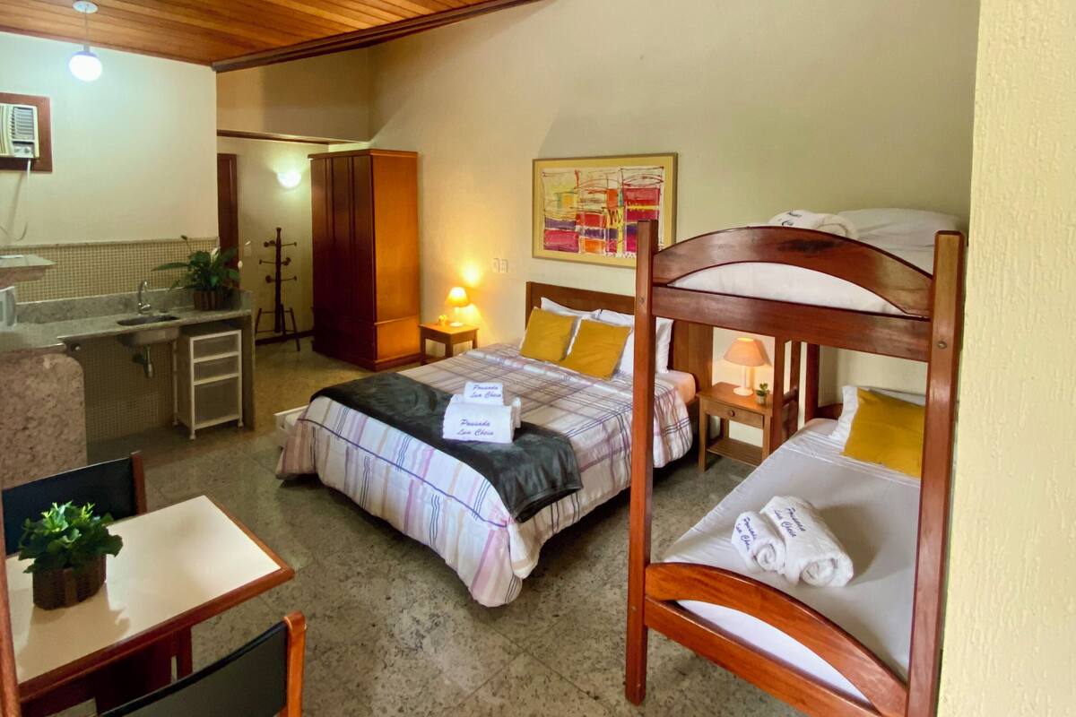 A bedroom with a bunk bed, a desk with a chair, a small kitchenette, and a ceiling fan.