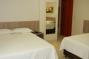 A hotel room with two beds, a bedside table with a remote control, and a painting on the wall. - Hotel Castro (Palmas)