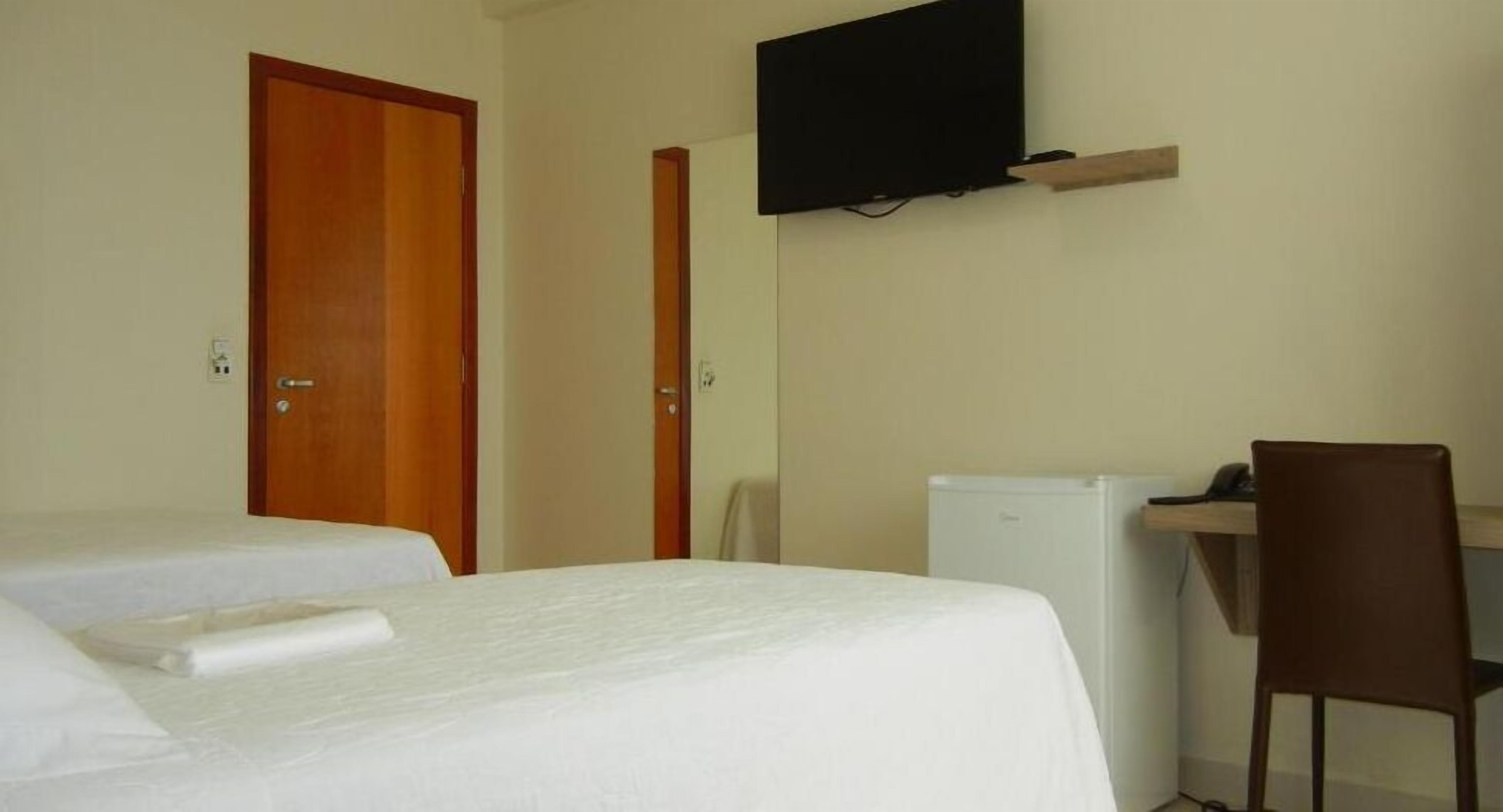 A hotel room with two beds, a desk with a chair, a television, and a refrigerator.