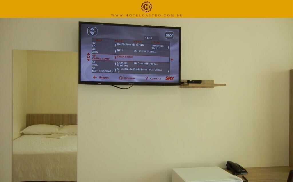 A hotel room with a television mounted on the wall displaying a TV guide.