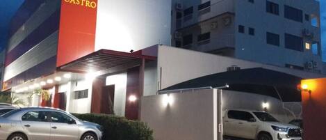 A hotel with a prominent red and white sign, a covered parking area, and two cars parked in front.