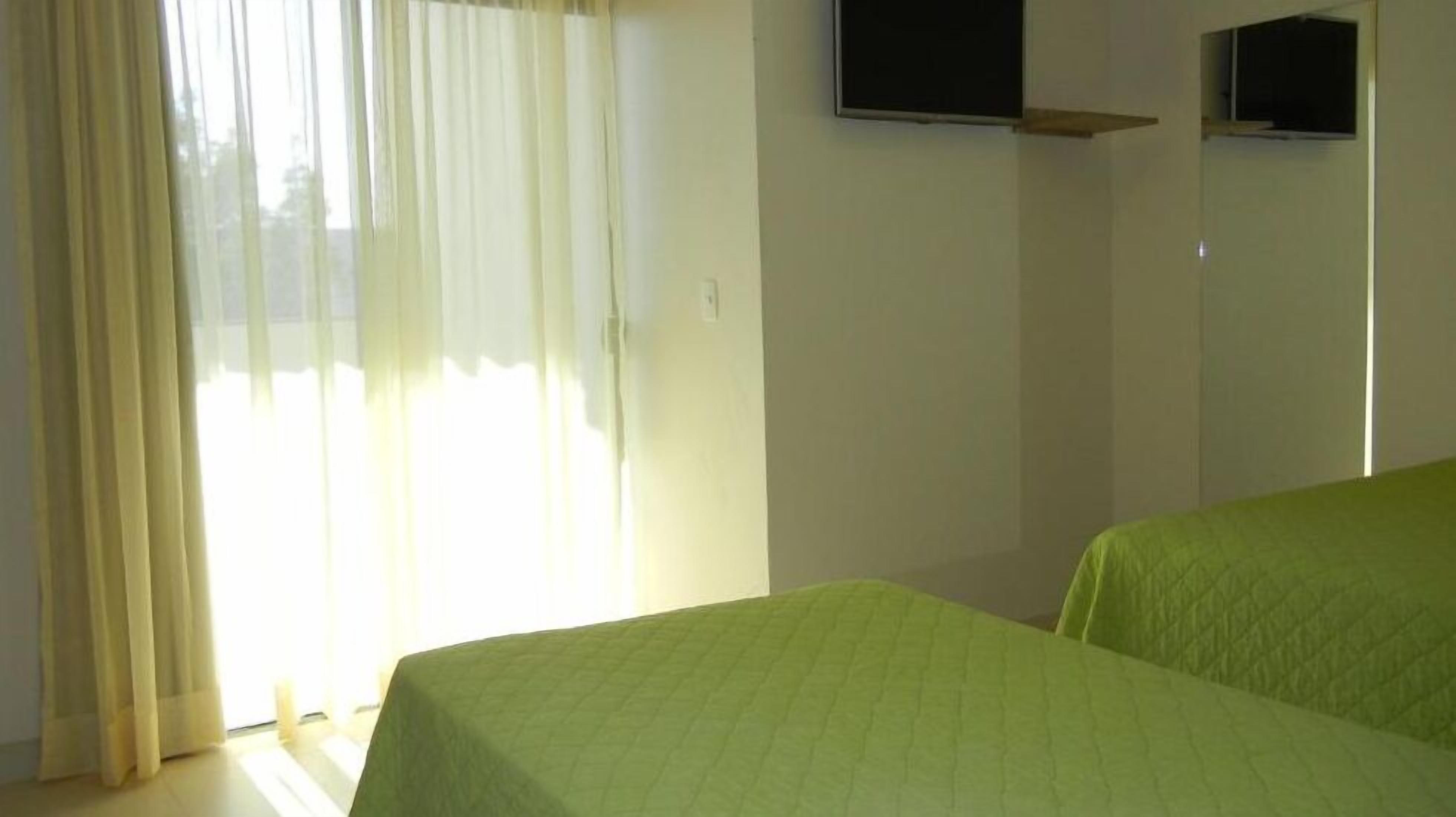 Una stanza con un letto, una TV a muro e una finestra con tende.