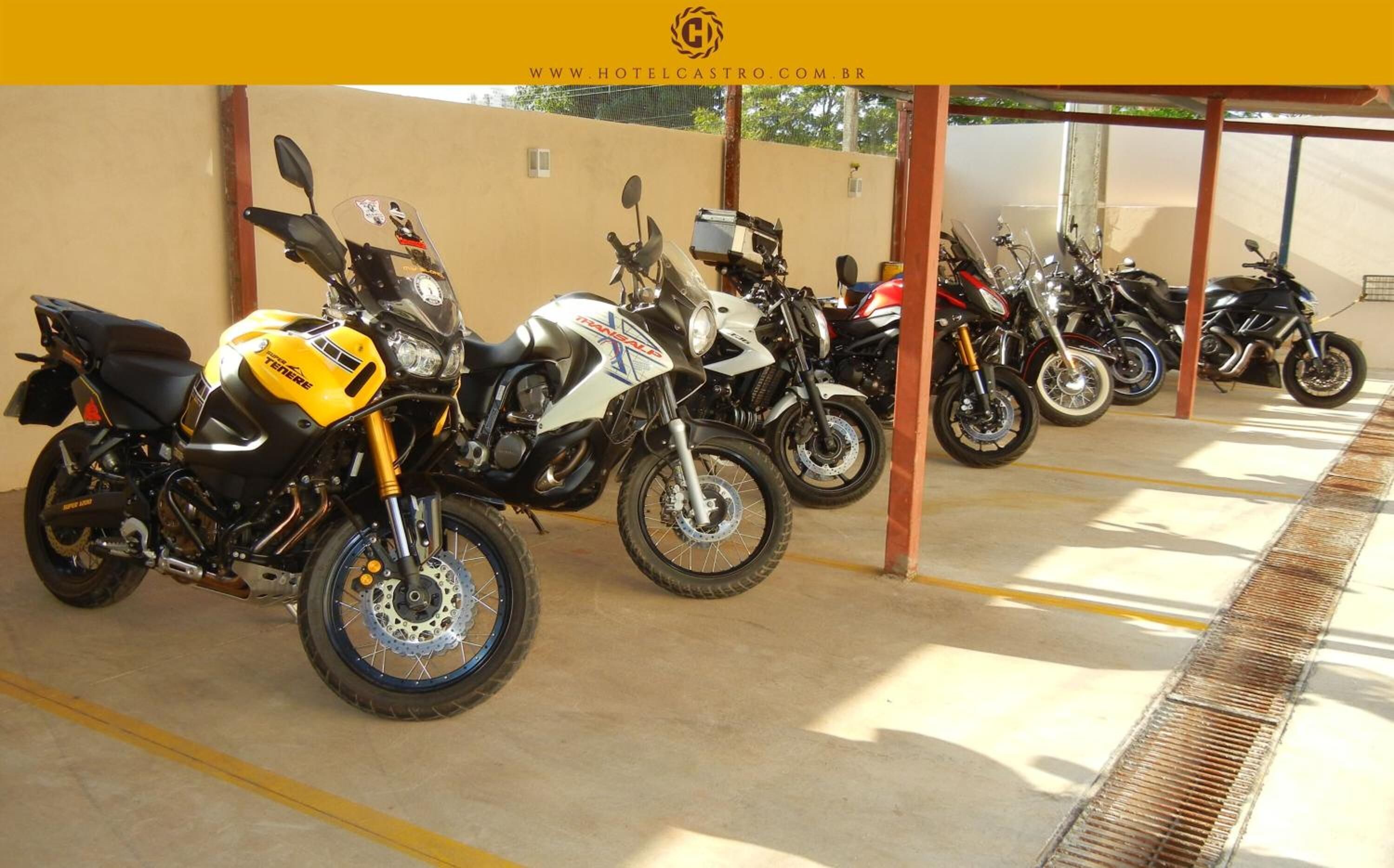 A row of motorcycles parked under a covered area with a concrete floor.