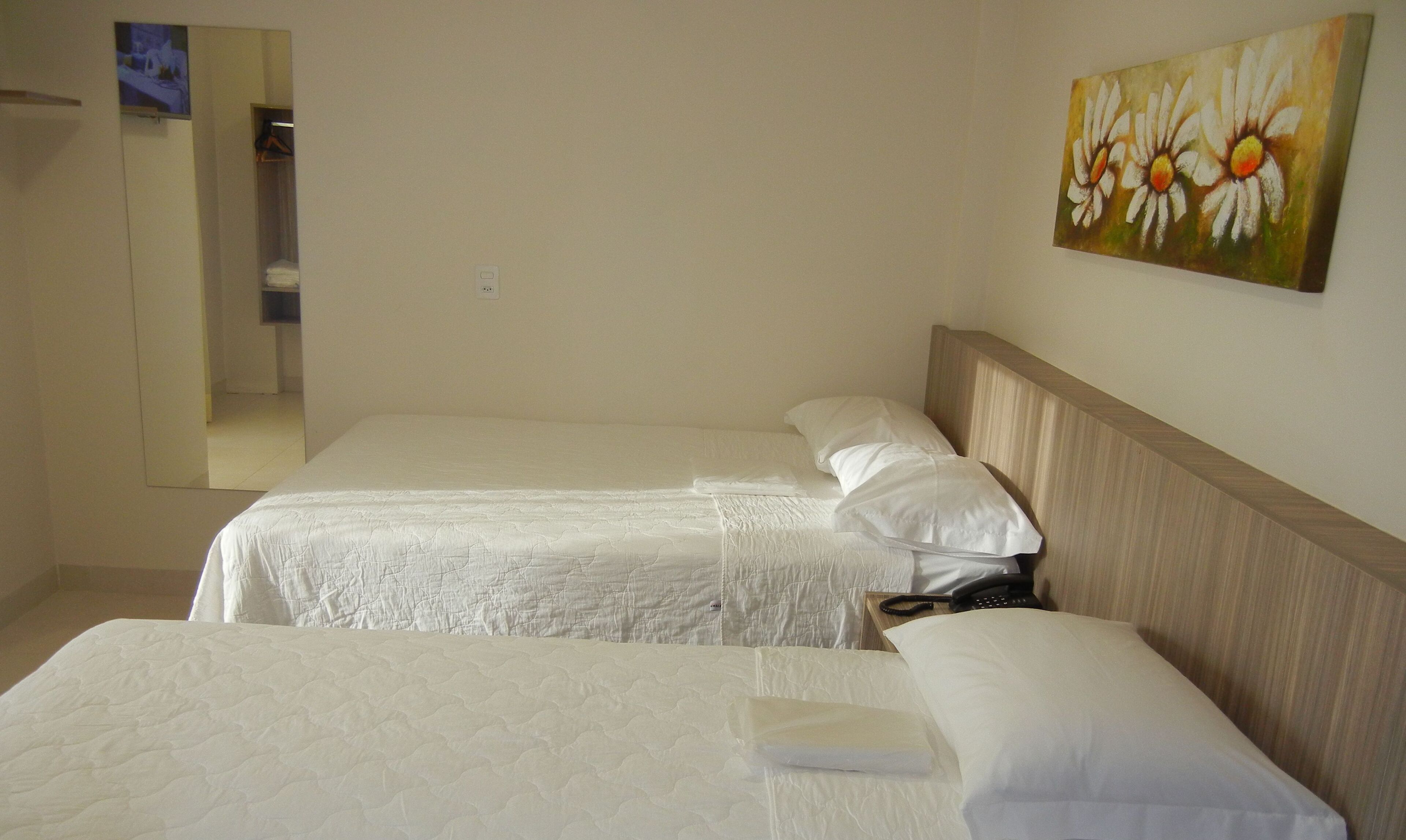 A hotel room with two beds, a wooden headboard, a painting of daisies, and a mirror on the wall.