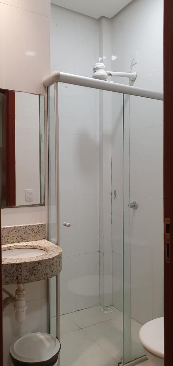 Un baño con cabina de ducha de vidrio, un lavabo con encimera de granito y un inodoro.
