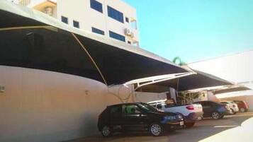 Uma área de estacionamento com um edifício branco e um carro preto estacionado sob uma cobertura.