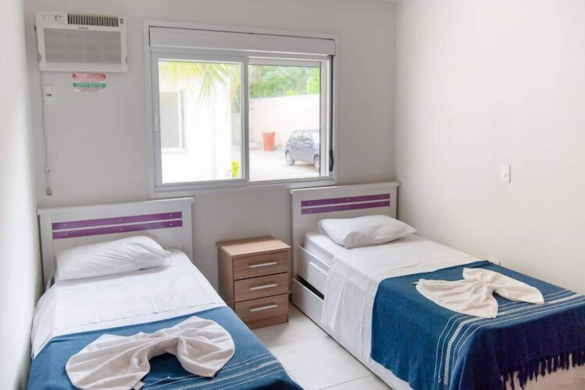 A twin room with two beds, a window, a heater, and a small wooden cabinet.