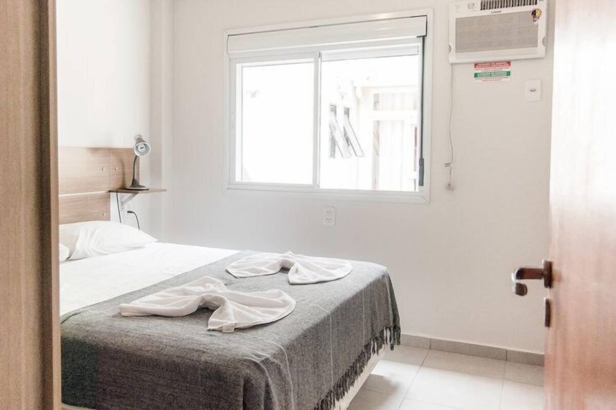 A hotel room with a bed, a window, and a door.