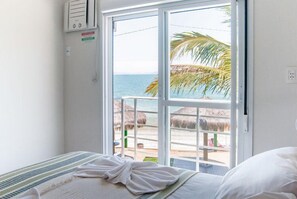 A hotel room with a bed, a window with a view of the beach, and a small air conditioning unit on the wall. - Pousada Holiday (Florianópolis)