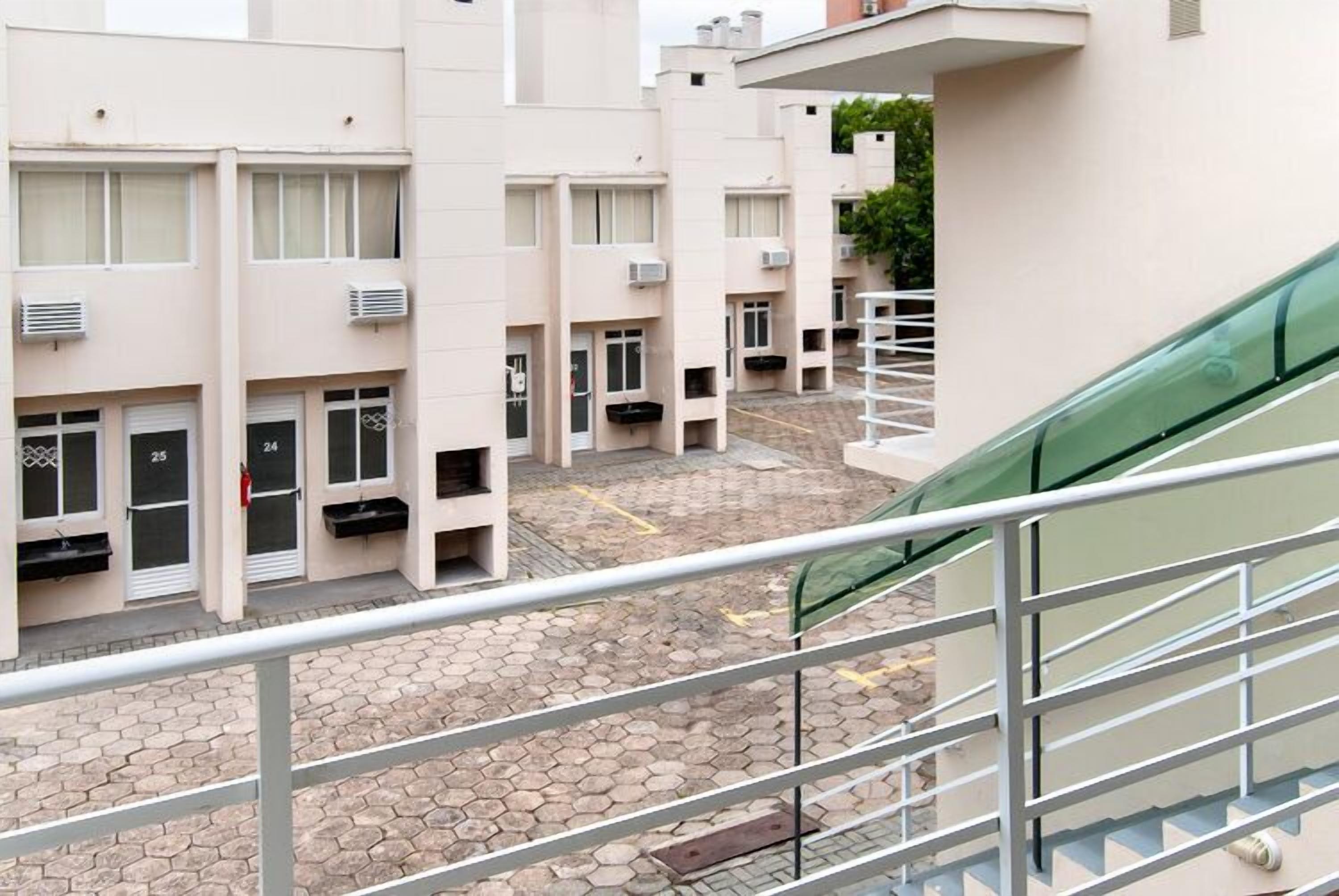 Um edifício residencial com várias varandas, um pátio pavimentado e um carro verde estacionado na rua.