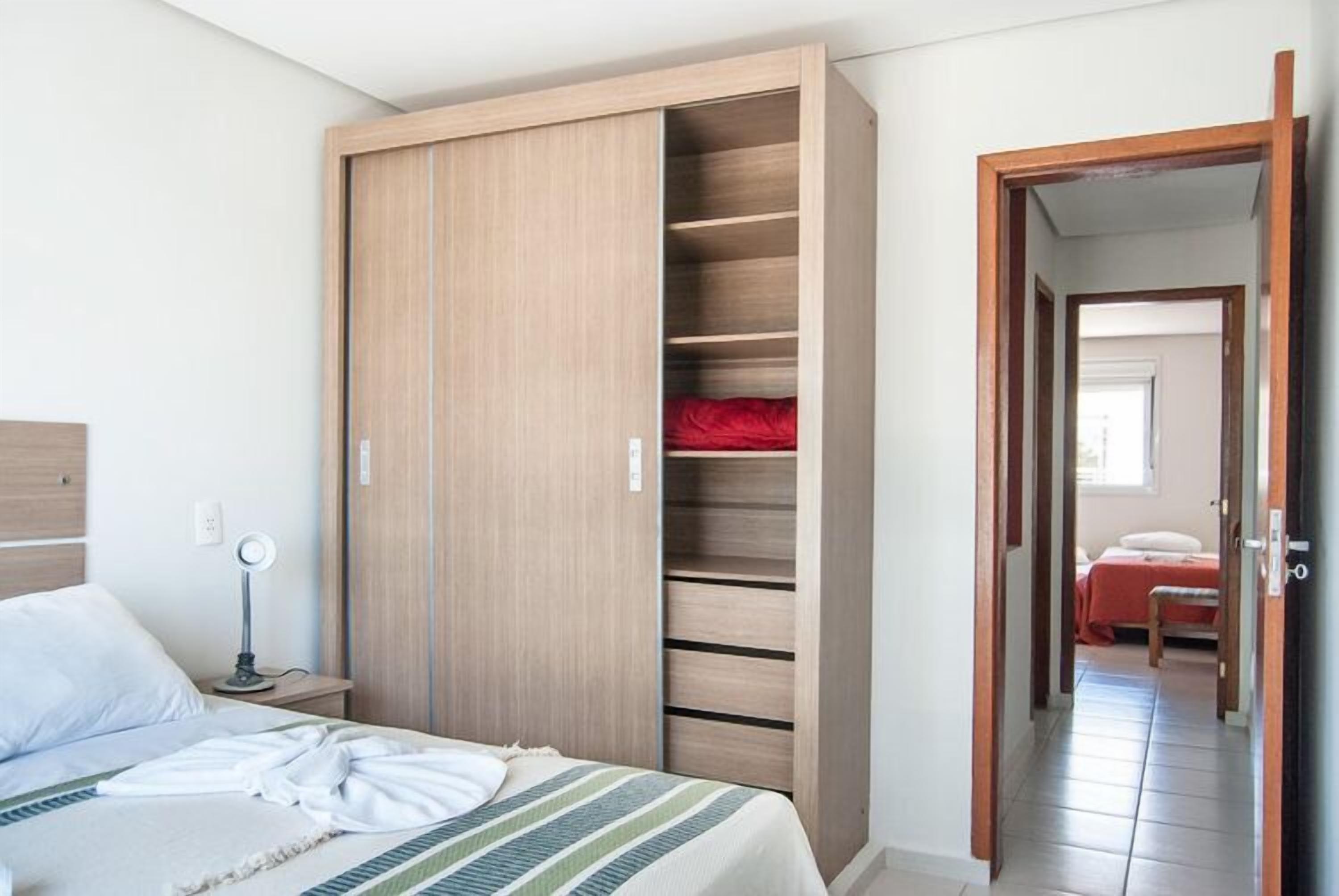 Un dormitorio con cama, mesita de noche y armario de madera con varios estantes.