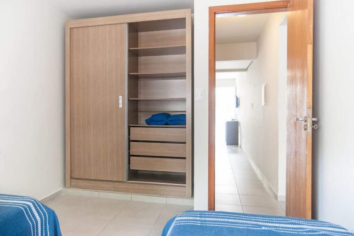 A room with a wardrobe, a bed, and a hallway leading to another room.