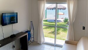 Habitación de hotel con televisión, escritorio, silla, sofá, puerta corredera de vidrio a un área de piscina y vista al océano.