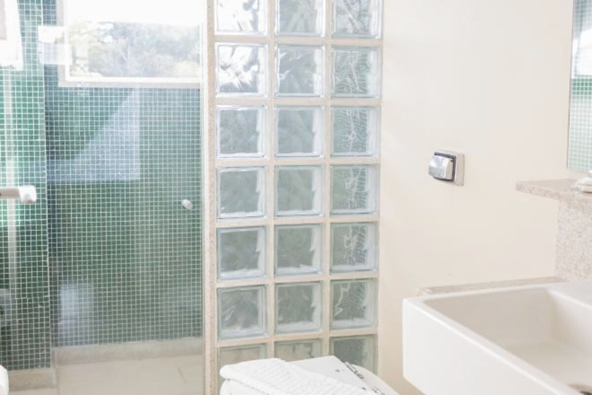 Un baño con ducha, bañera y ventana con vista a árboles.