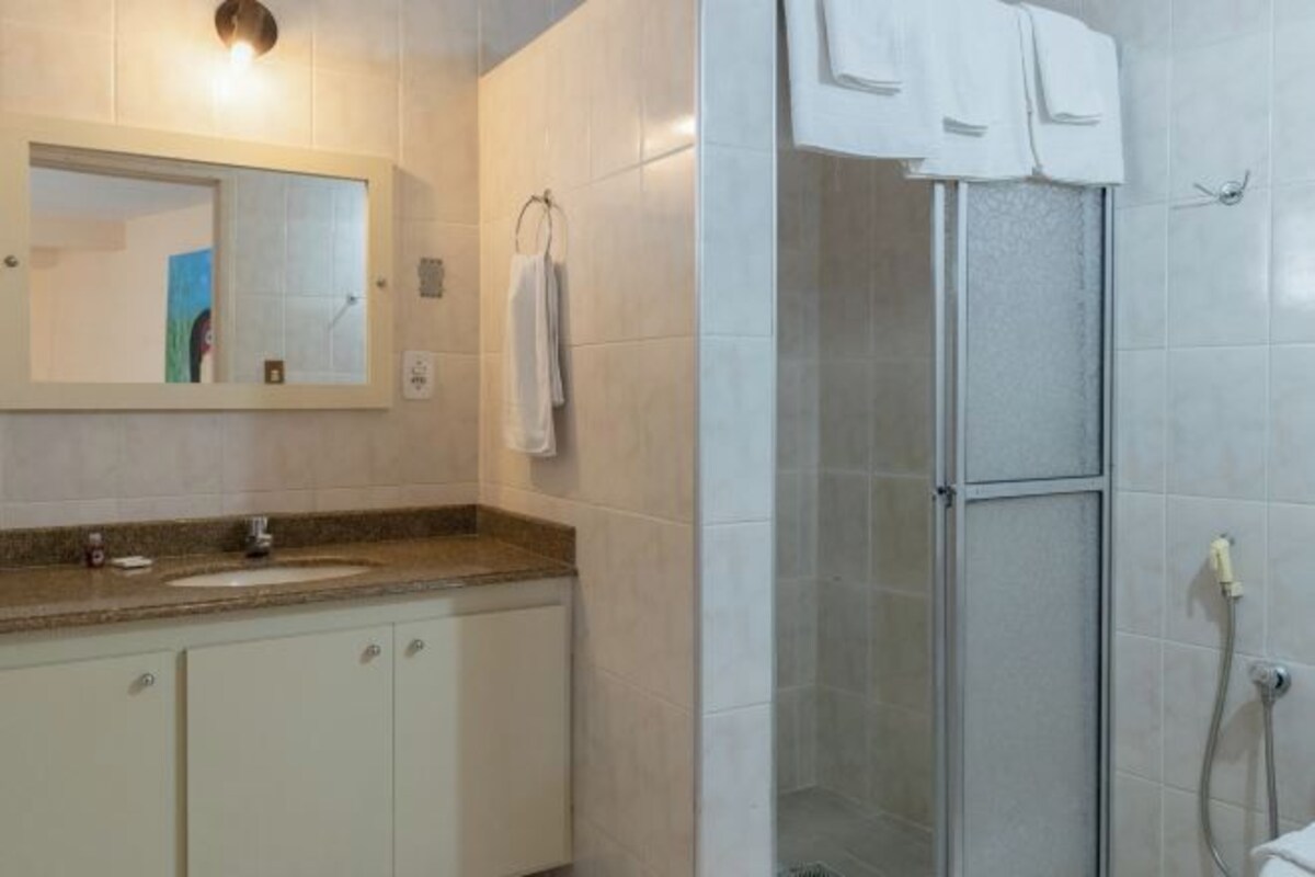 Un baño con lavamanos, espejo y zona de ducha con mampara de vidrio.
