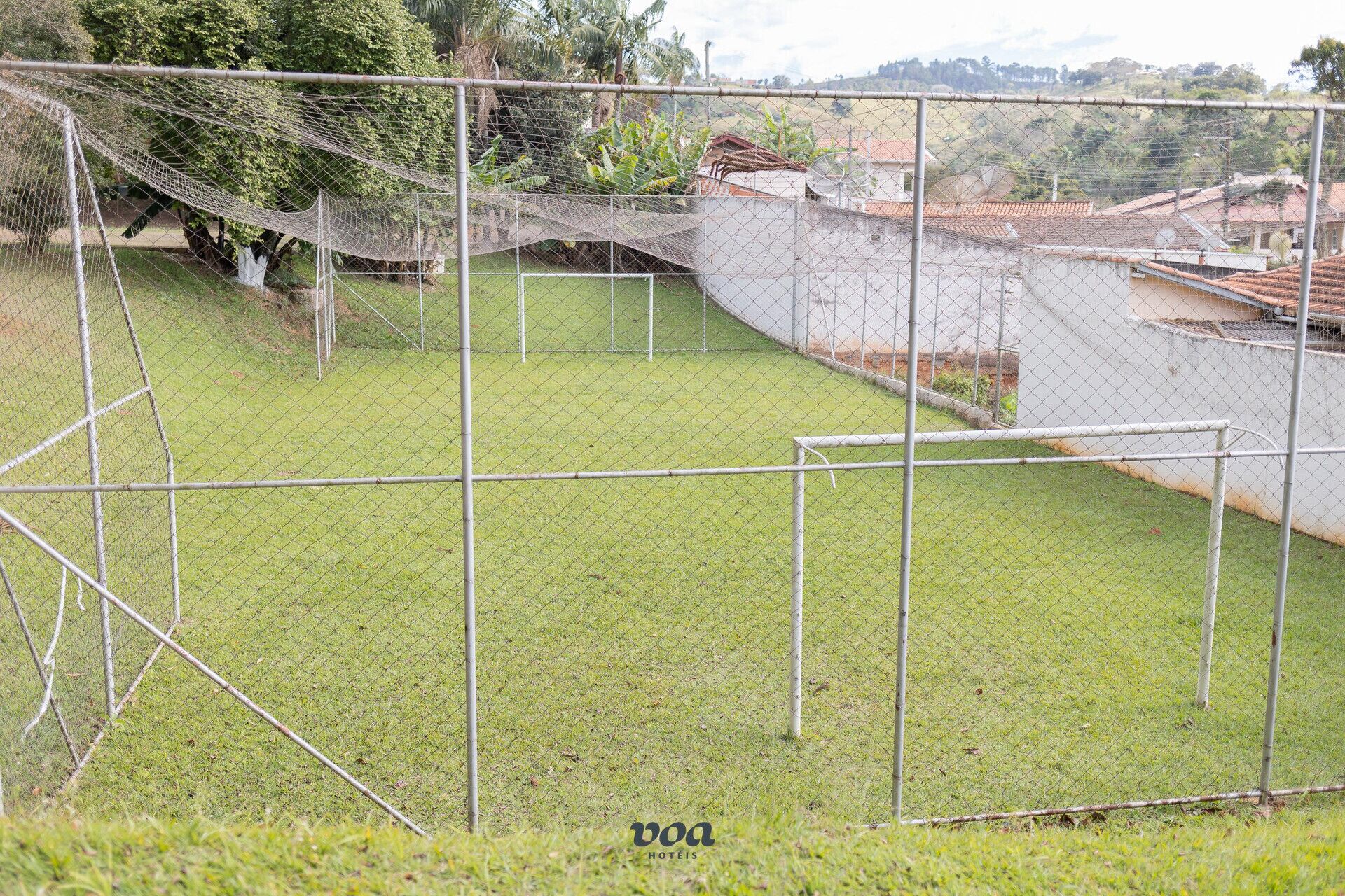 A fenced outdoor area with a grassy field, a soccer goal, and a netted play area.