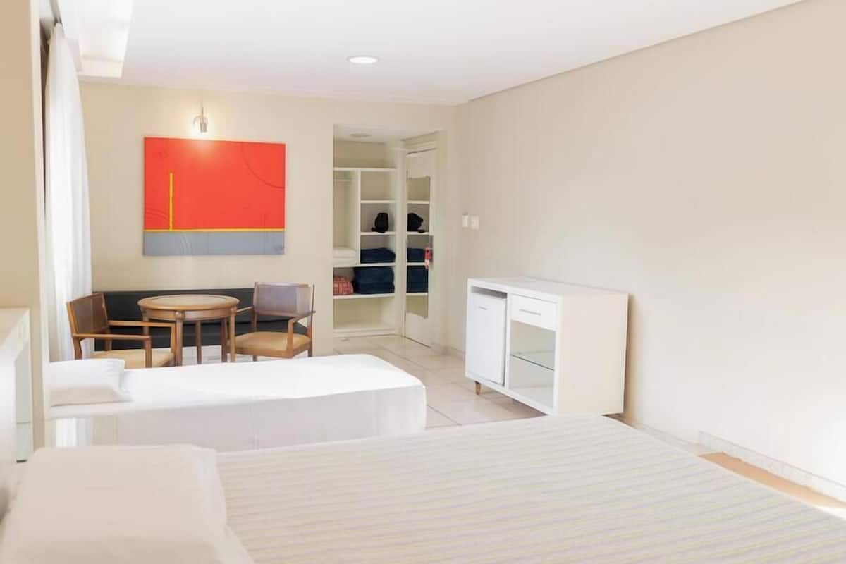 A hotel room with two beds, a desk, a chair, a wardrobe, and a red abstract painting on the wall.