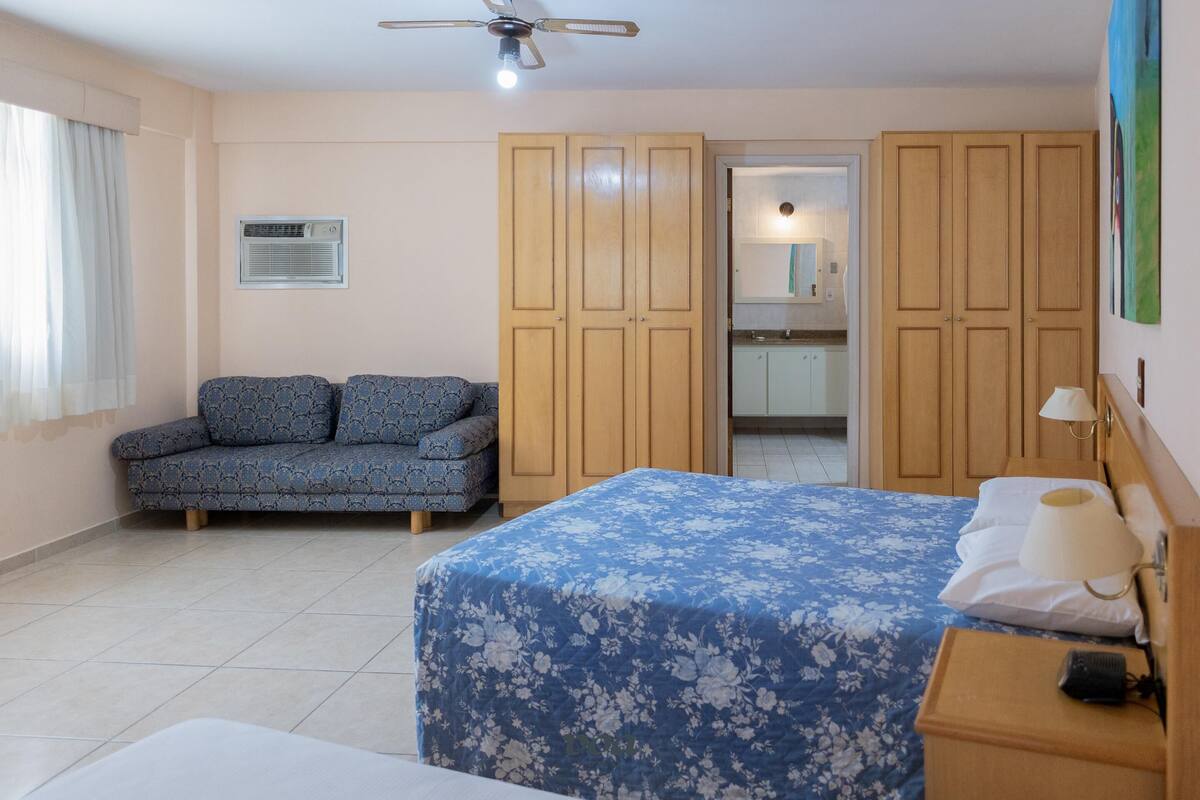 A bedroom with a bed, a sofa, a wardrobe, and a ceiling fan.