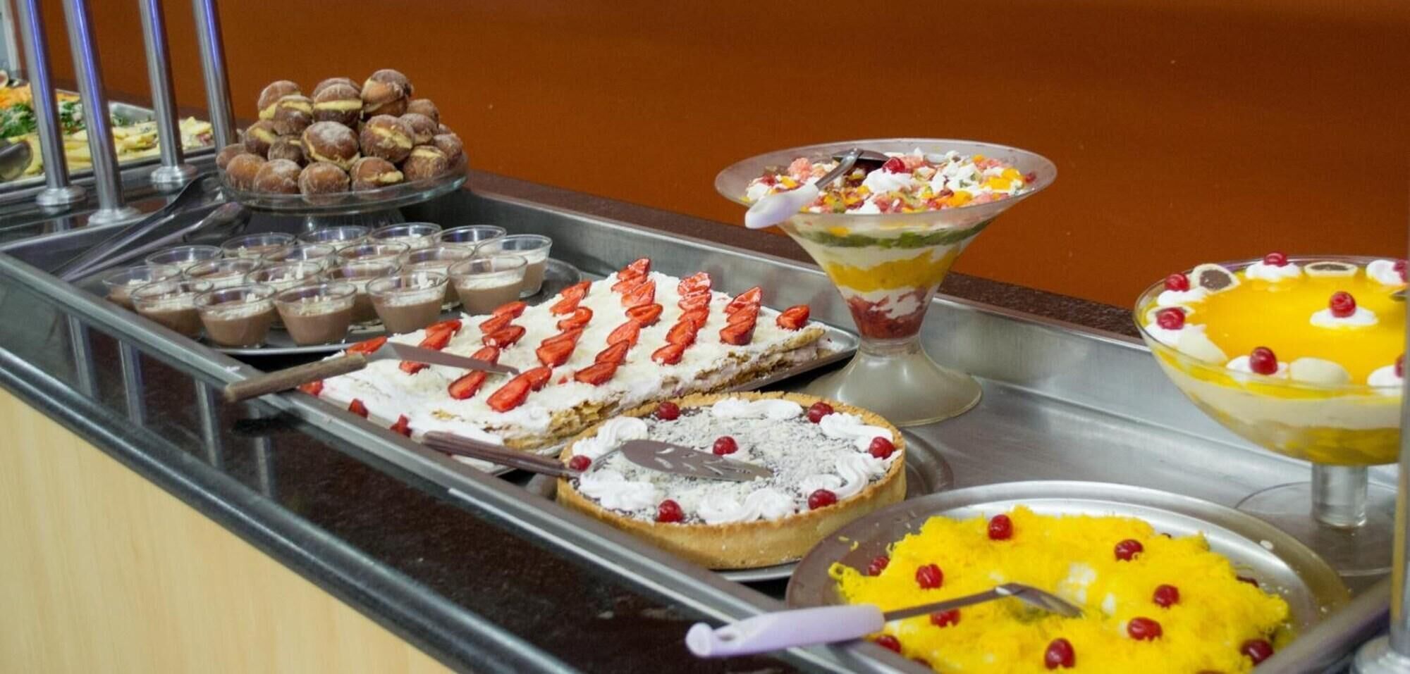 Un bufé con diversos postres, incluyendo tartas, pasteles y platos a base de frutas.
