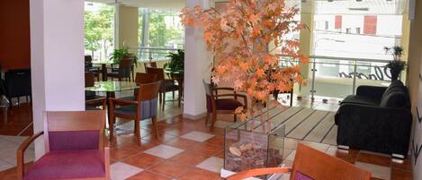 A spacious lobby with a glass coffee table, wooden chairs, a sofa, and a decorative plant.