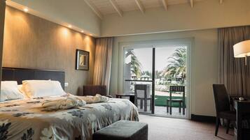 Habitación de hotel con cama, escritorio y vistas a un jardín con palmeras.