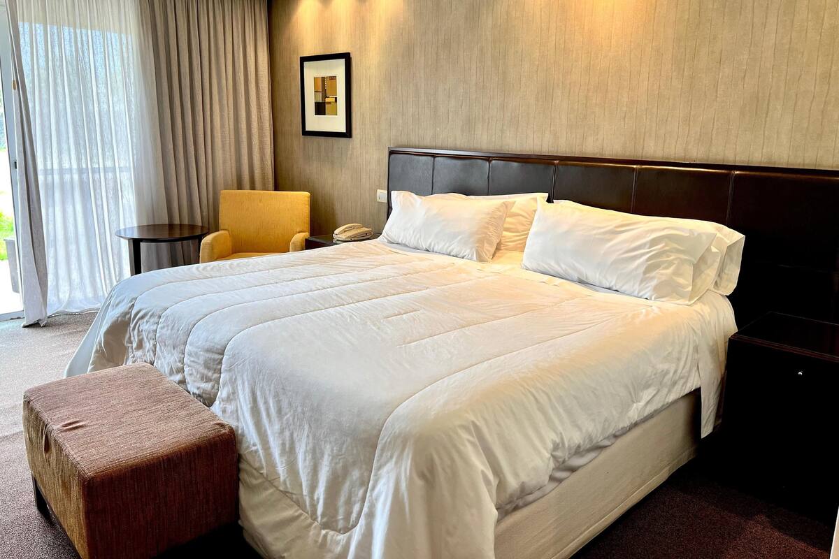 Ein Hotelzimmer mit einem großen Bett, einem Nachttisch, einem Sessel und einem Bild an der Wand.