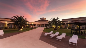 A hotel courtyard with lounge chairs, palm trees, and a building with a tiled roof.