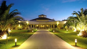 A hotel entrance with a central pathway, palm trees, and illuminated lights.