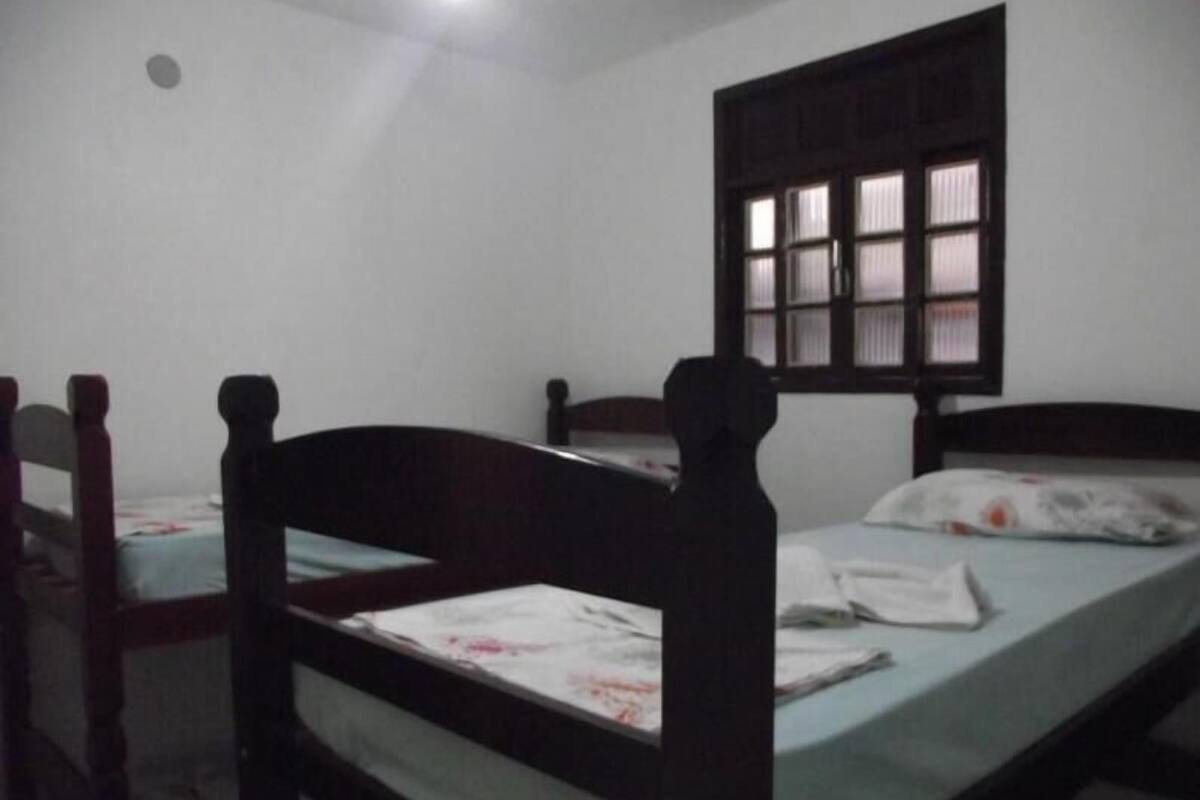 A simple room with two single beds, a window with a wooden frame, and a plain white wall.
