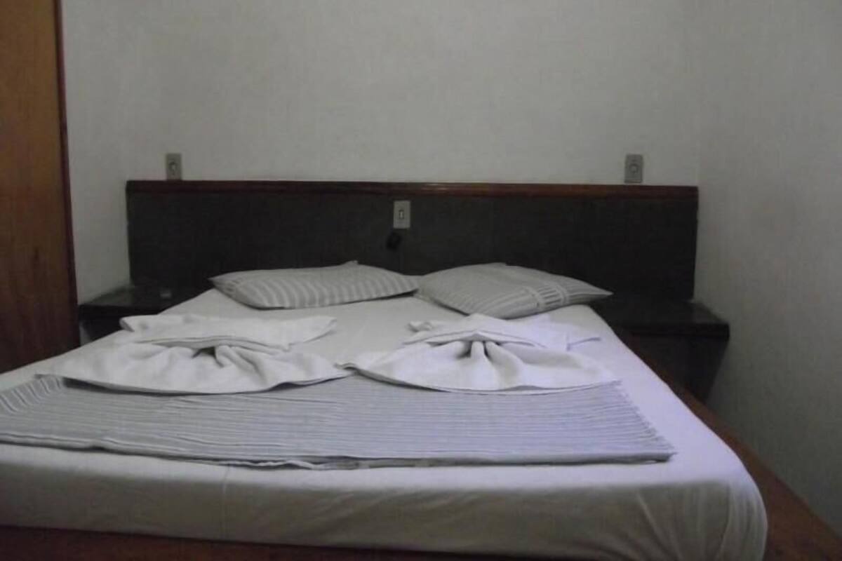 A neatly made bed with pillows and a folded blanket, a wooden headboard, and a plain wall.