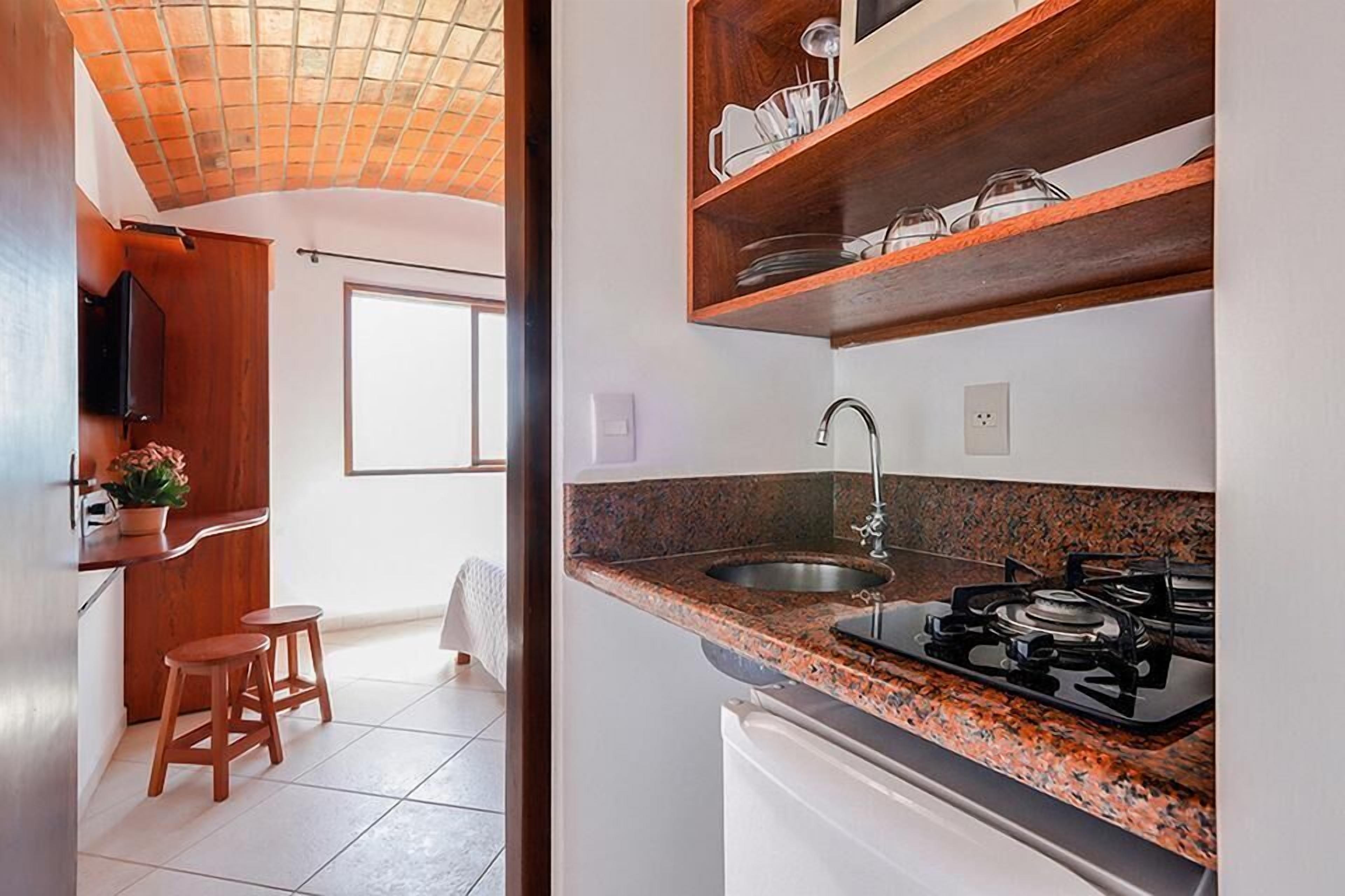 A kitchen with a granite countertop, stainless steel sink, and a gas stove. There are wooden stools and a potted plant.