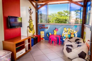 A children's playroom with a TV, colorful furniture, and wall murals of 'The Simpsons'. - Village Paraíso (Florianópolis)