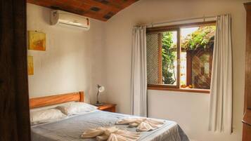 A bedroom with a bed, a nightstand, a lamp, a window with curtains, and an air conditioning unit.