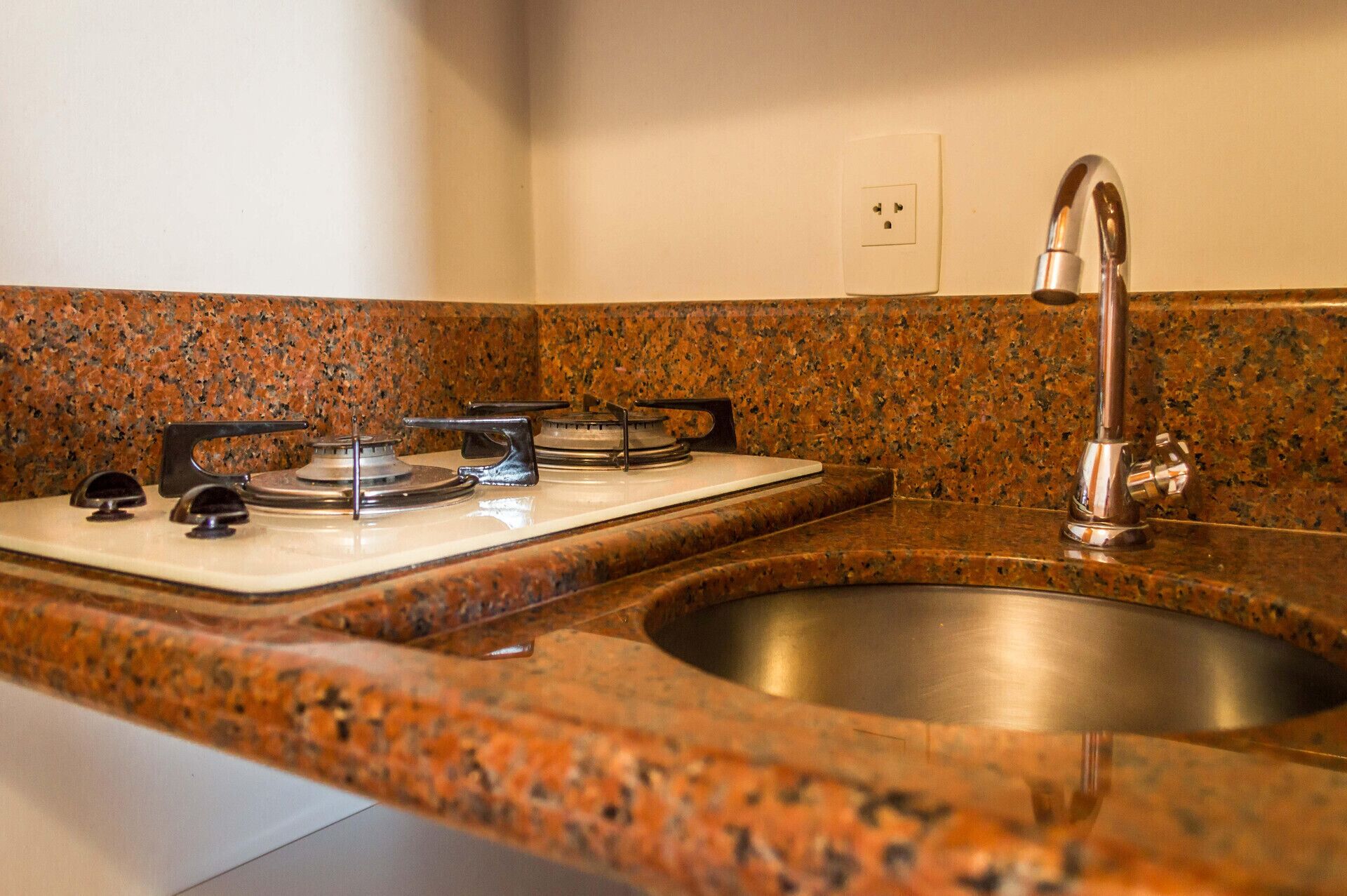 A kitchen with a granite countertop, stainless steel sink, and a gas stove.