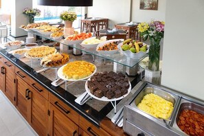 A buffet with various food items and a vase of flowers. - Village Paraíso (Florianópolis)