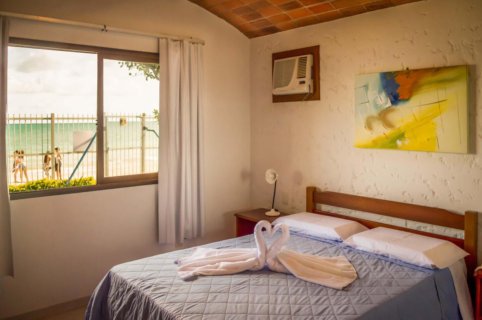 Une chambre d’hôtel avec un lit, une fenêtre donnant sur la plage, un tableau au mur et un appareil de climatisation.
