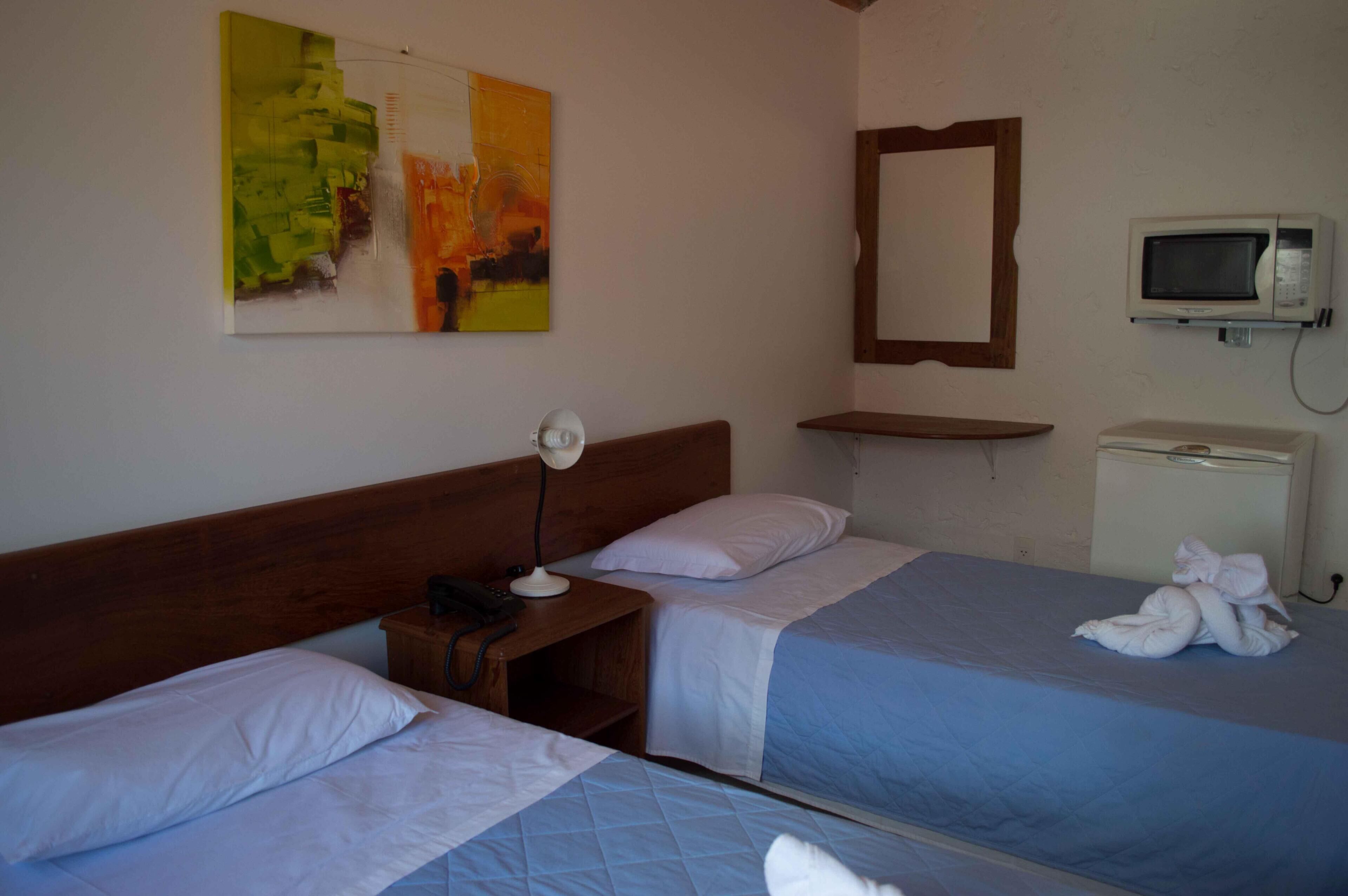 A hotel room with two beds, a bedside table with a lamp, a television, and a mirror.