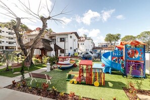 Ein Spielplatz mit Rutschen und Klettergerüsten, umgeben von einem gepflegten Rasen und einem Gebäude mit rotem Dach.