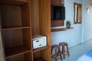 Una habitación con estanterías de madera, un televisor montado en la pared, una pequeña planta en maceta y dos taburetes de madera.