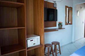 A room with wooden shelving, a television mounted on the wall, a small potted plant, and two wooden stools. - Village Paraíso (Florianópolis)