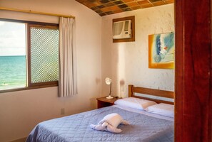 Una habitació d'hotel amb un llit, una finestra que dona al mar, un aparell d'aire condicionat i un quadre a la paret.