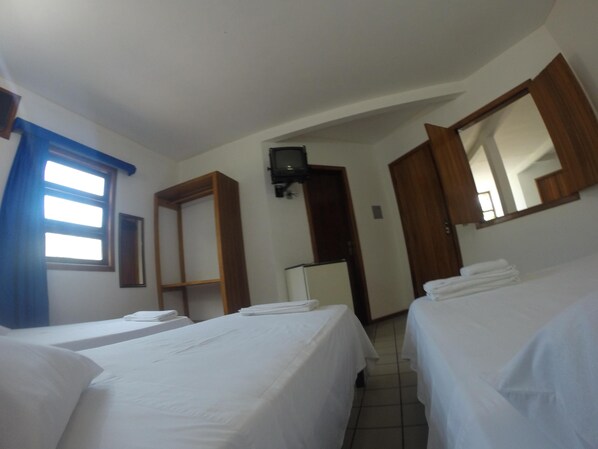 Una habitación con dos camas, un armario de madera, un espejo, un televisor y una ventana con cortinas.