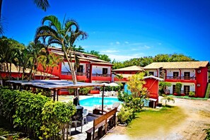 A resort with a swimming pool, outdoor seating, and red buildings. - Hotel Marilia (Porto Seguro)