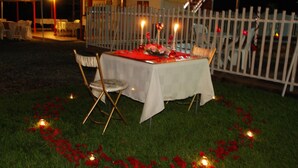 An outdoor dining area with a table set for two, surrounded by a white fence and decorated with red rose petals and candles. - Finca Hotel Fatima (Armenia)