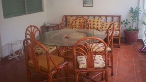 Zona pranzo con tavolo rotondo in vetro circondato da sedie in vimini con sedili imbottiti.