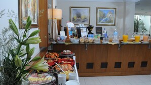 A buffet area with various food items, a coffee station, and framed artwork on the wall.