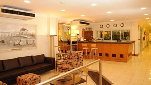 A hotel lobby with a reception desk, a sofa, a patterned armchair, and a painting on the wall.