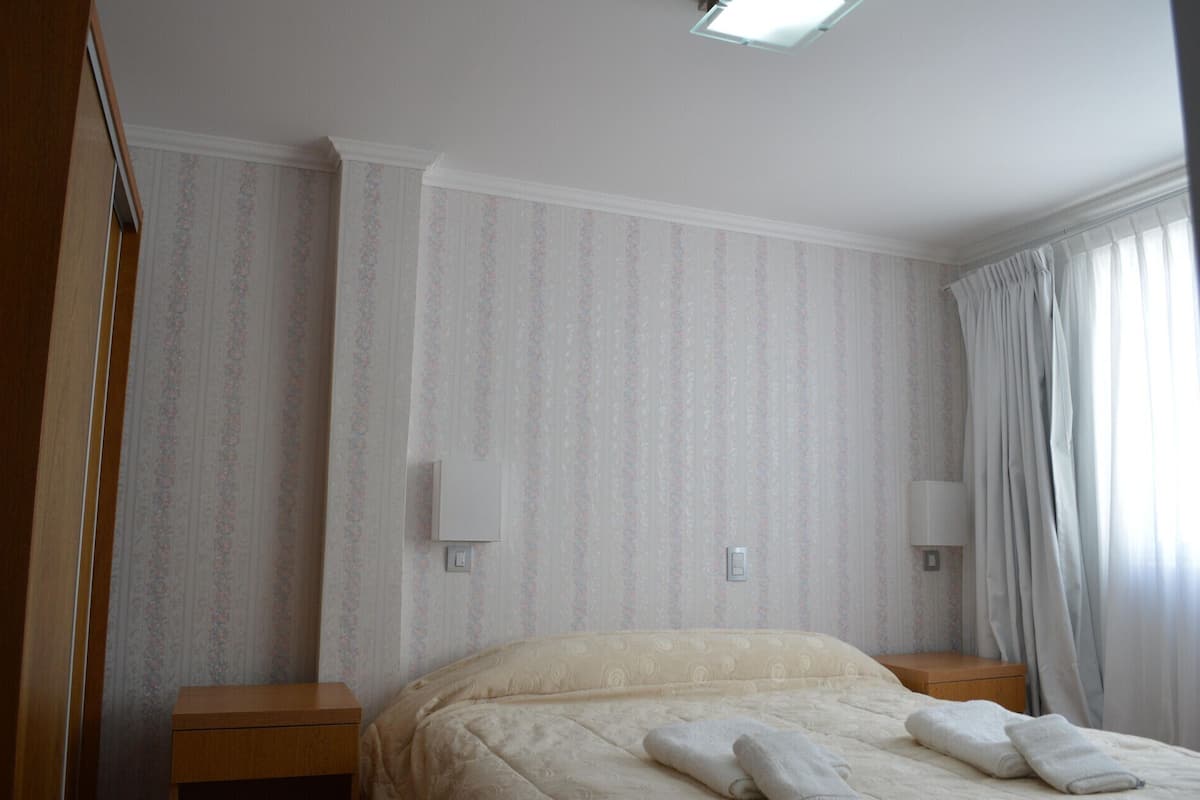 A hotel room with a bed, two bedside tables, and a window with curtains.