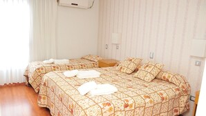 A double bed with floral bedding, a bedside table, and a window with curtains.