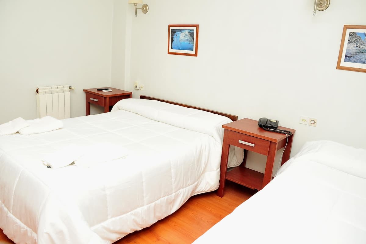 A hotel room with a large bed, a bedside table with a telephone, and a wall-mounted picture.